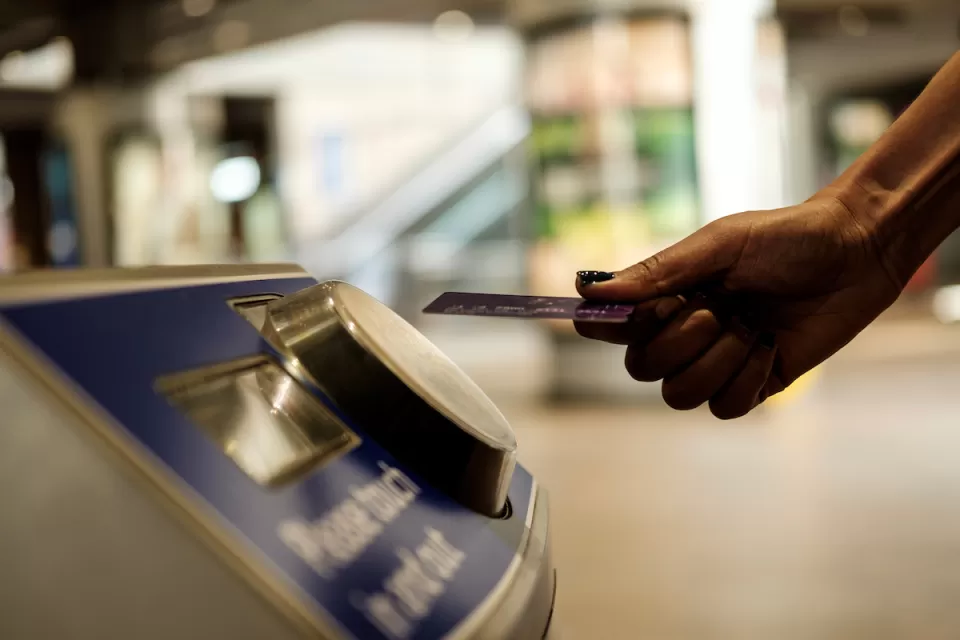 Close-up of hand holding transit card up to fare collection machine in transit station.